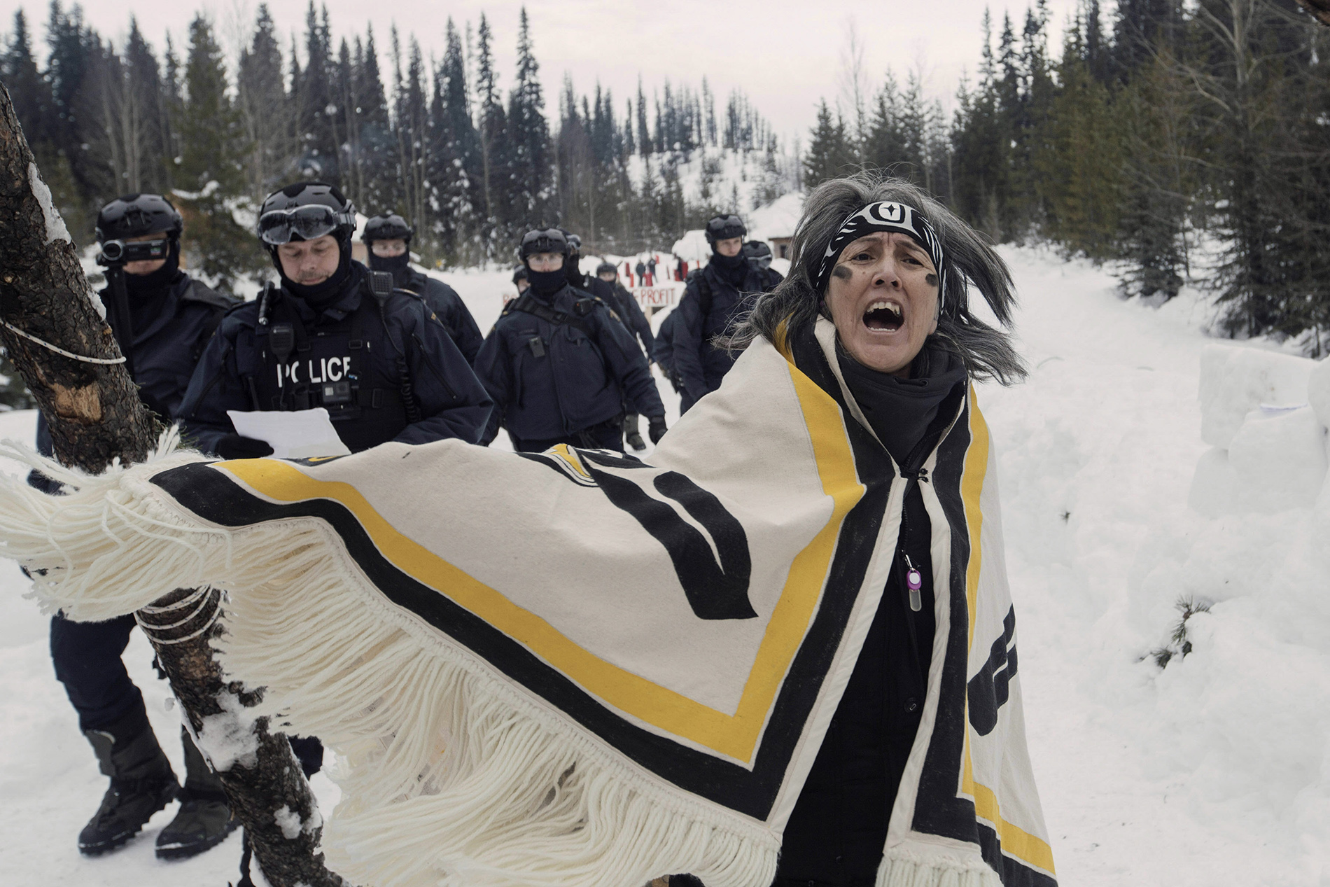 Chief Howilhkat, Freda Huson, stands in ceremony while police arrive to enforce Coastal GasLink’s injunction at Unist’ot’en Healing Centre .These images are licensed for promotion and publicity of the documentary feature film ‘Yintah’ . Any usage beyond the purpose of reviewing or commenting on the film, including reporting related to the subject matter, is unauthorized copyright infringement subject to fees and damage costs. © Amber Bracken